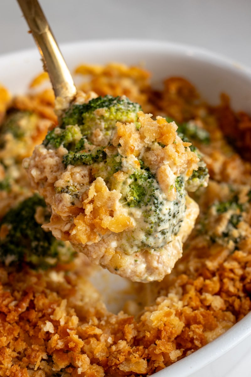 a golden spoon holding a scoop of broccoli casserole.