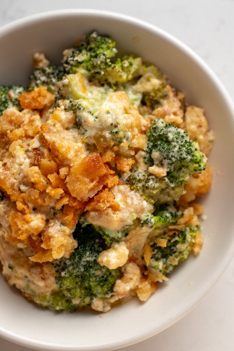 a close up of a small white bowl filled with cheesy broccoli casserole.