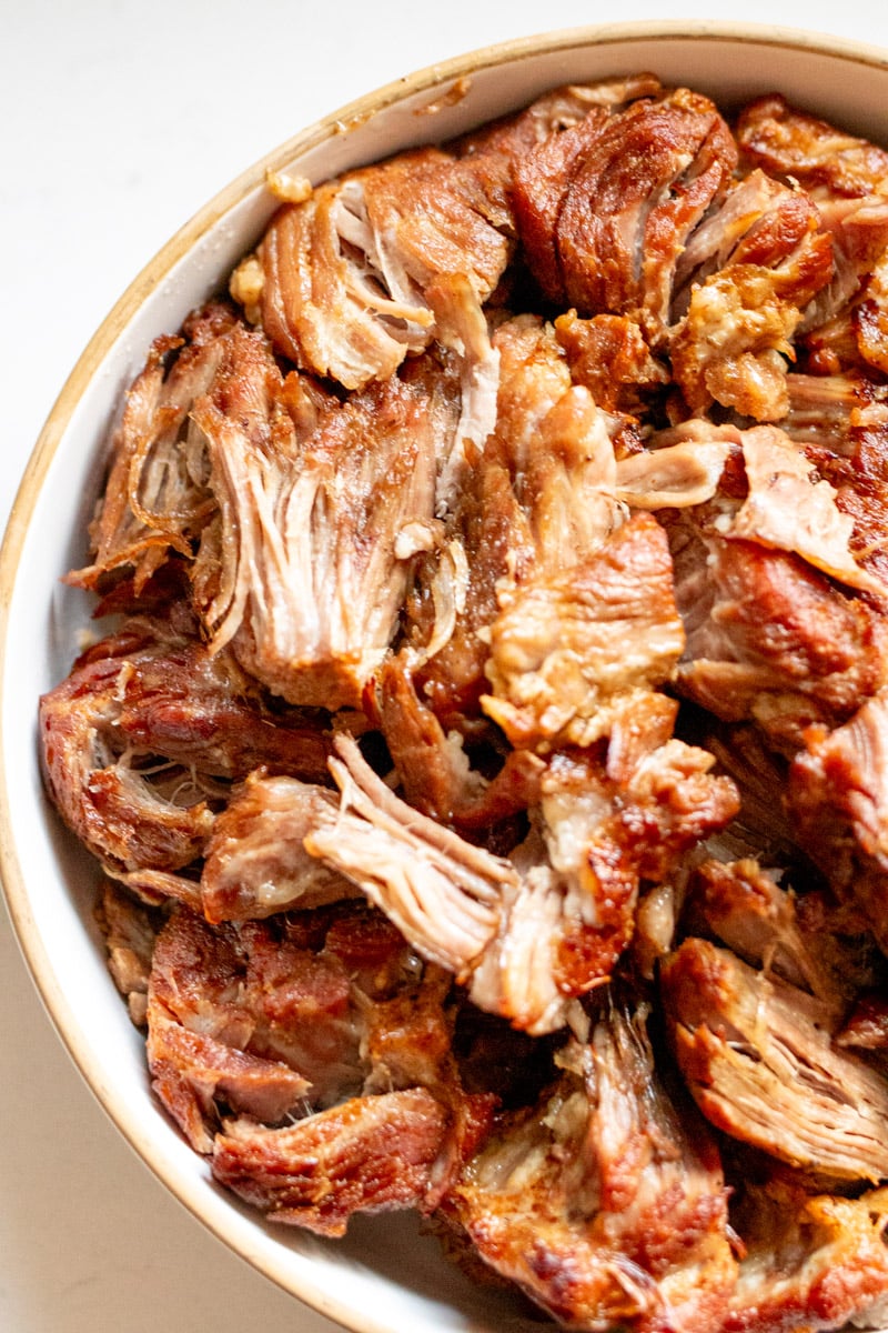 the left side of a white platter filled with pulled pork that was cooked in an instant pot.