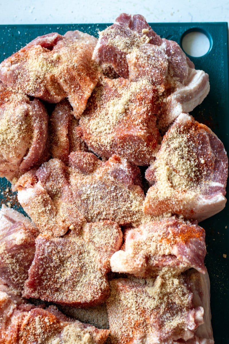 chunks of pork butt covered in spices on a blue cutting board.