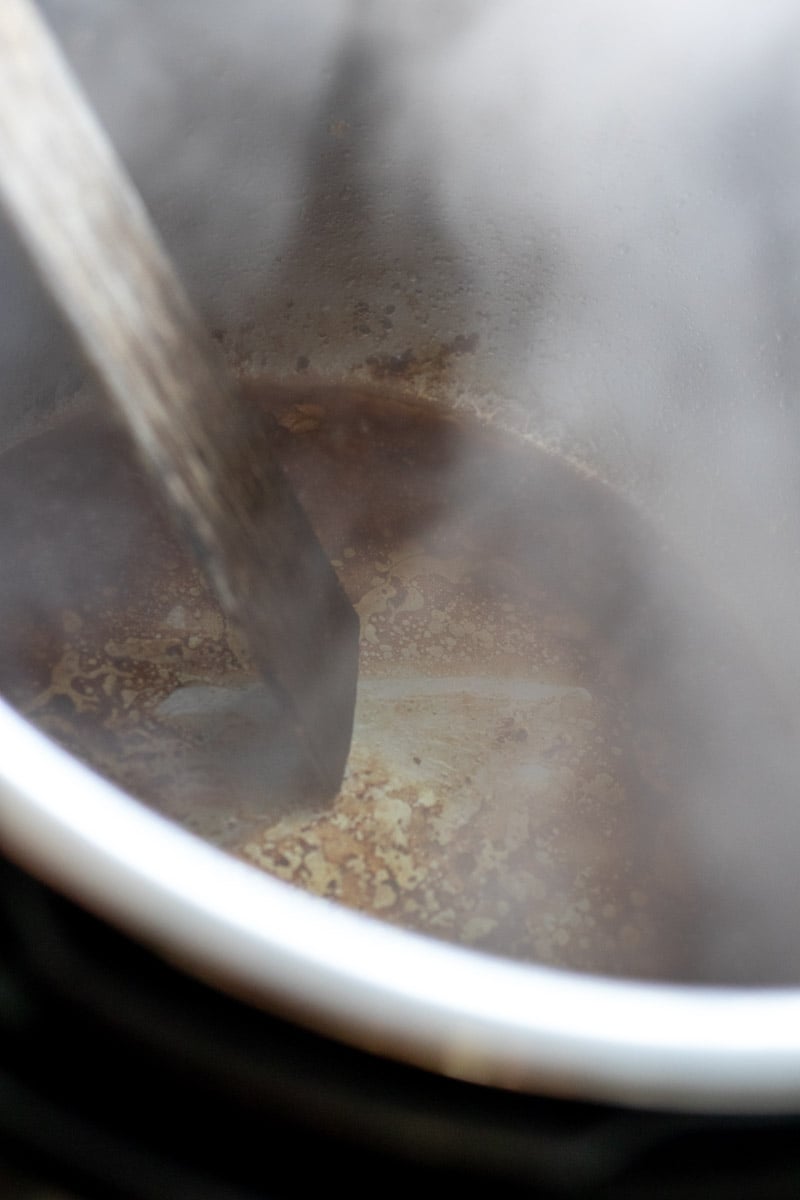 a flat spatula scraping up all the brown bits at the bottom of an instant pot.