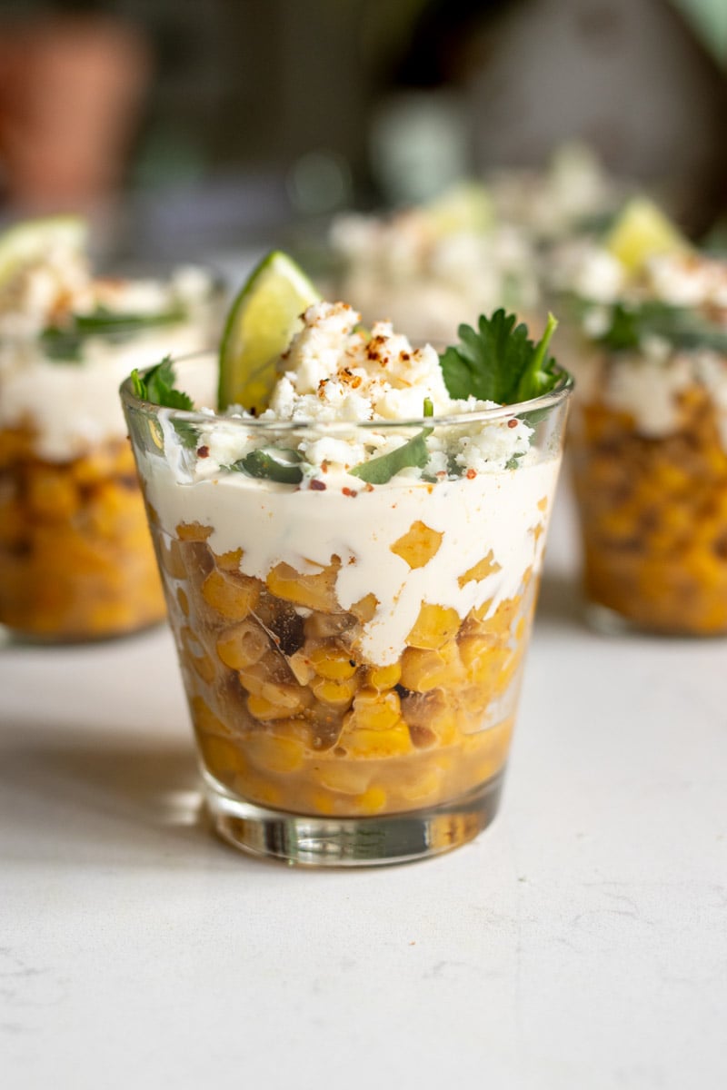 a few glass cups filled with mexican elote in a cup.