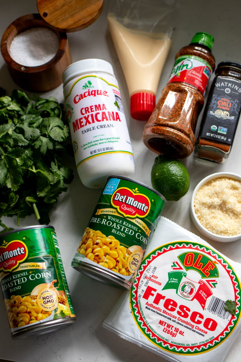 all of the ingredients needed to make elote in a cup on a white countertop.