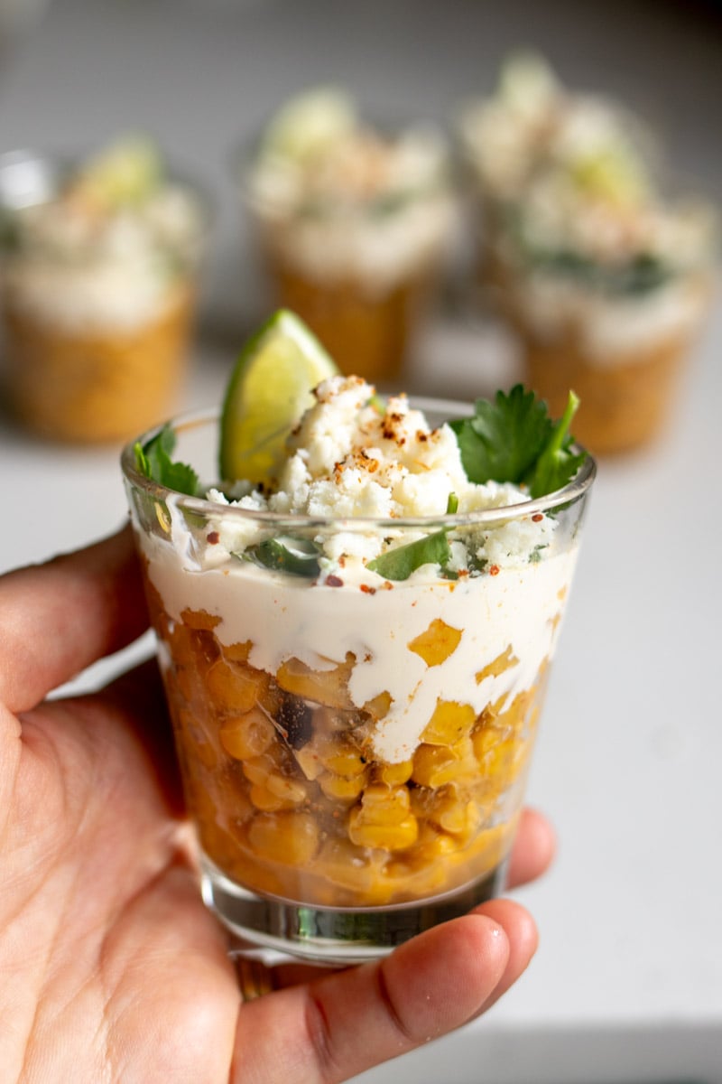 a hand holding a single elote in a cup. 