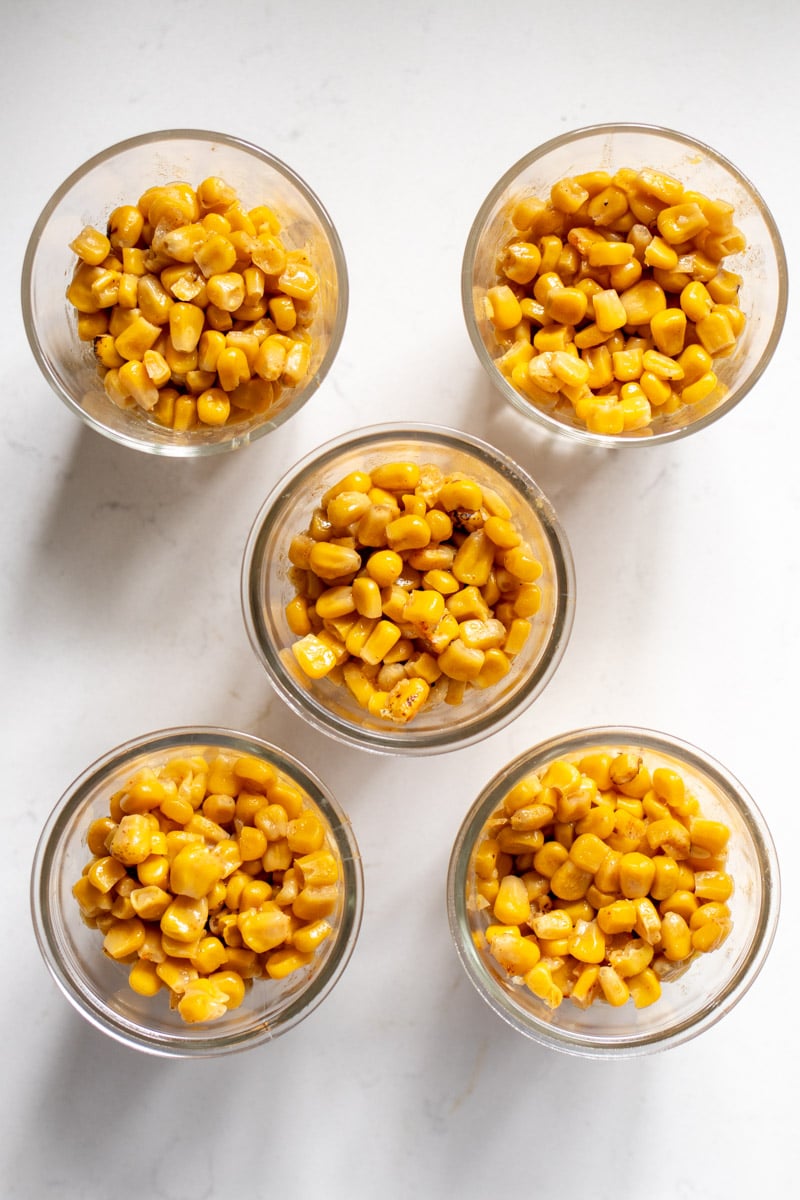 Mexican street elote in glass cups on a white countertop.