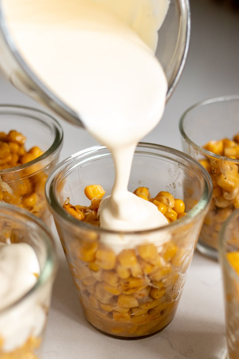 crema being poured into cups filled with esquites. 