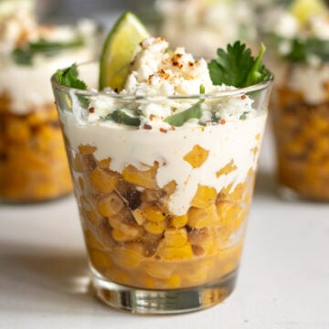 Elote in a glass cup with sour cream and lime on top.