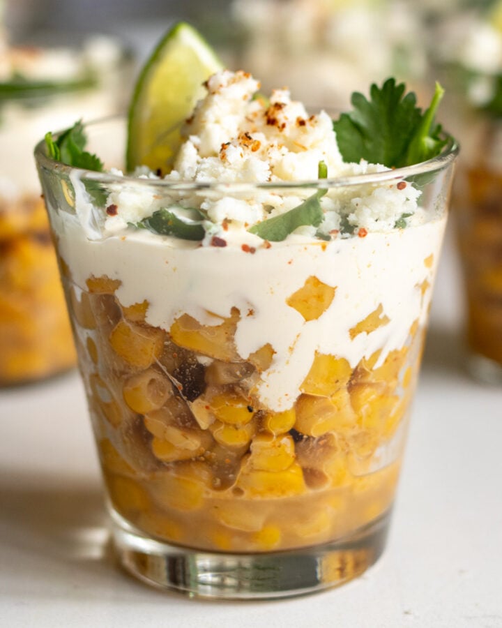 Elote in a glass cup with sour cream and lime on top.