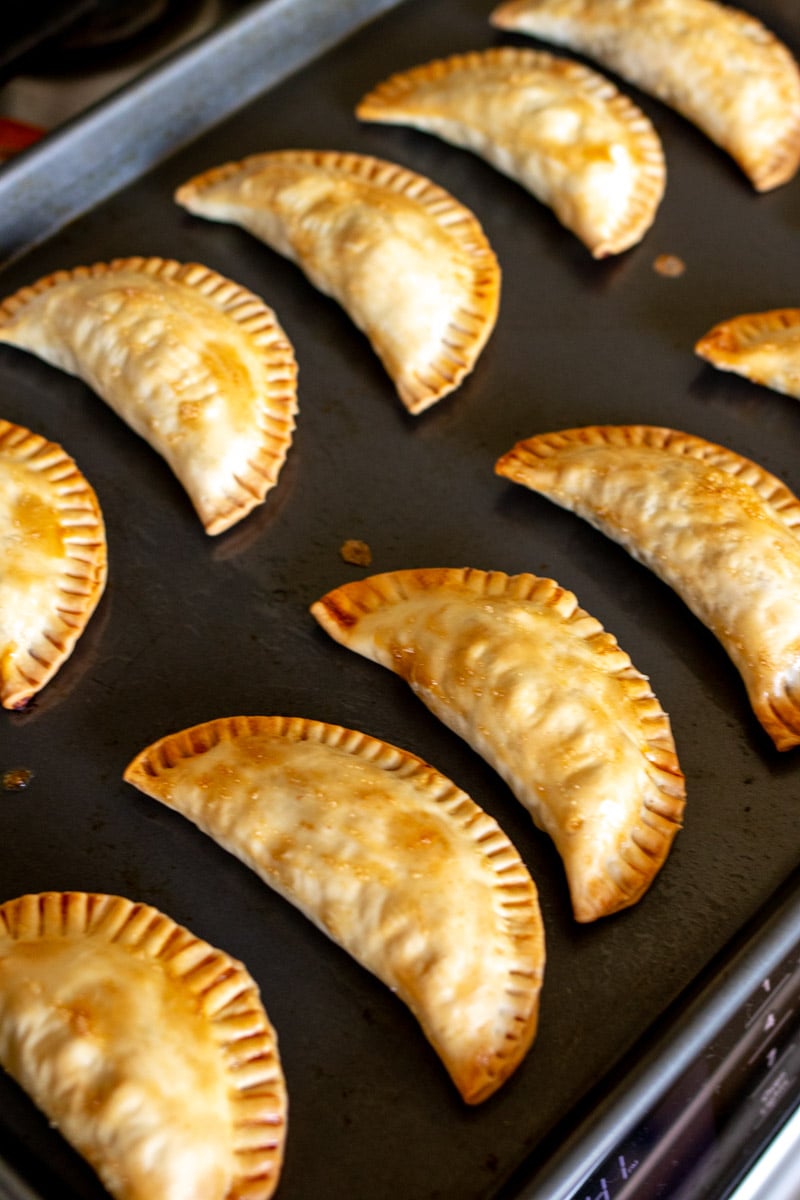 baked empanadas lined up on a baking sheet. 