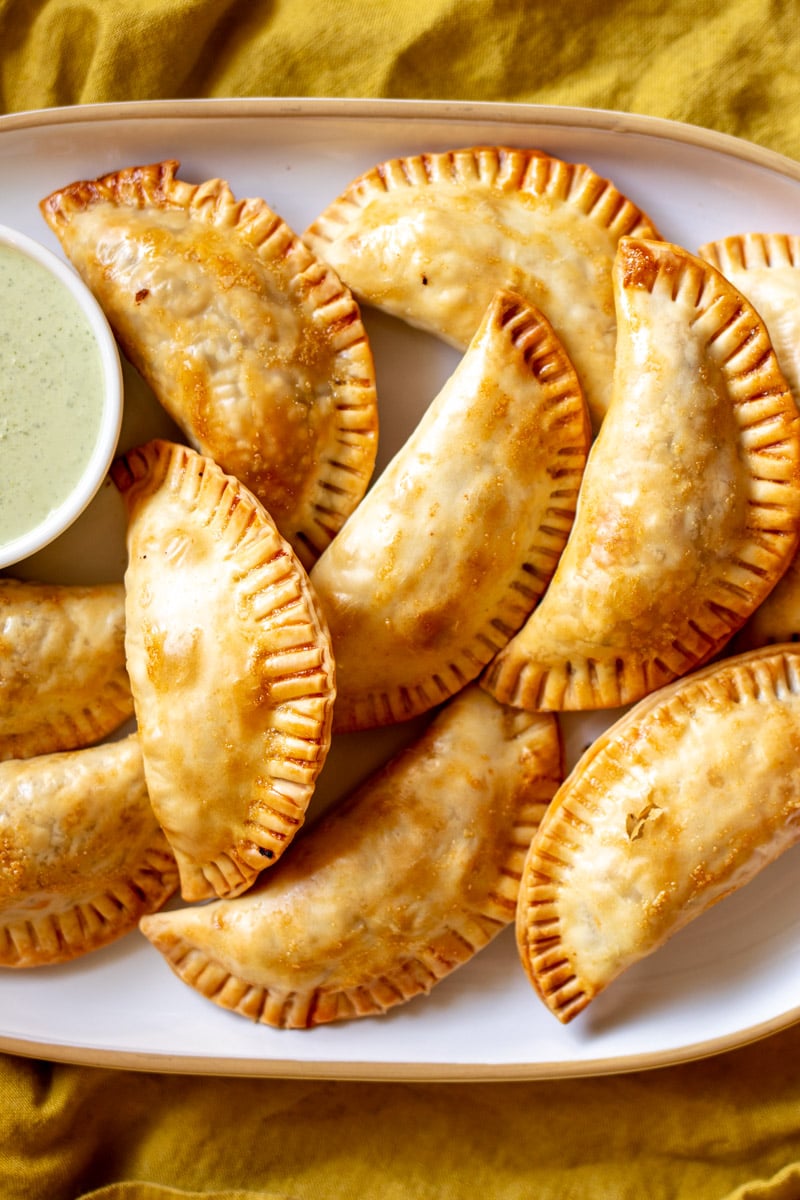 a close up of a platter of baked empanadas with cilatnro sauce. 