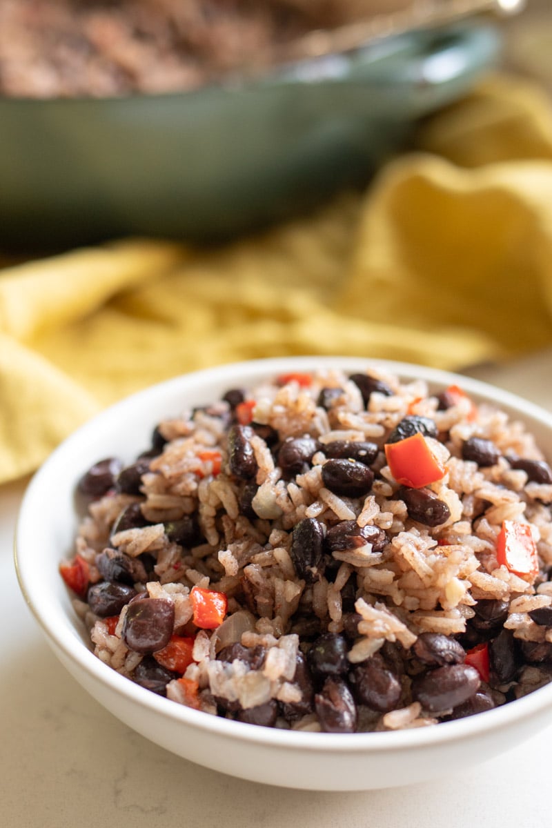 a white bowl of black beans and rice with a yellow napkin and a blue pot behind it.