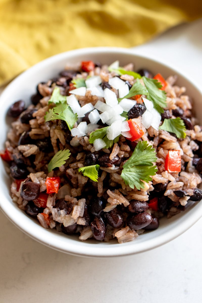 a white serving bowl filled with black beans and rice, onion, cilantro and tomato.