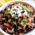 a white bowl filled with black beans and rice that's topped with onion, cilantro and tomato.