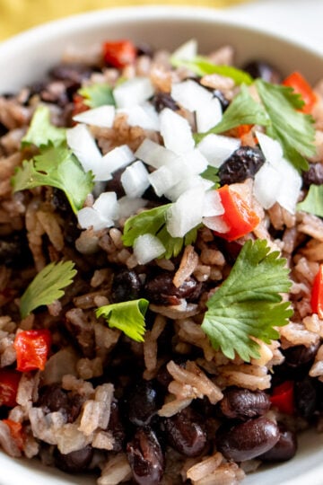 a white bowl filled with black beans and rice that's topped with onion, cilantro and tomato.