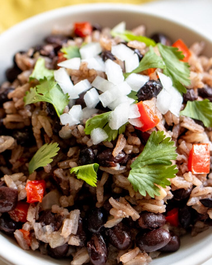 a white bowl filled with black beans and rice that's topped with onion, cilantro and tomato.