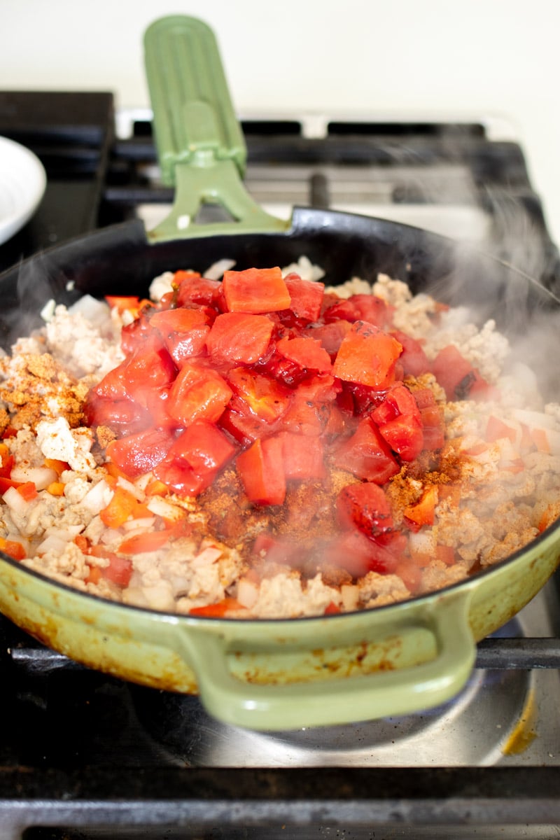 ground chicken cooking with tomatoes, peppers and sauce.