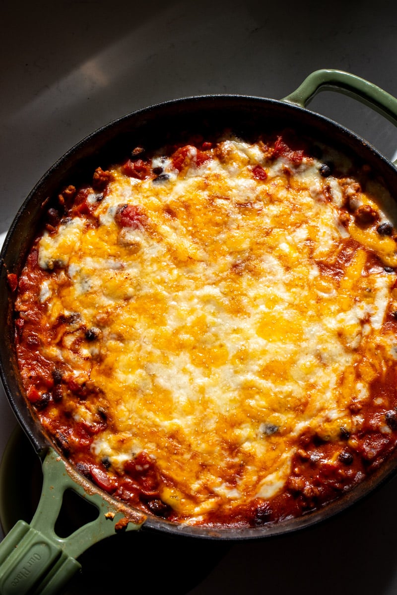 cheesy ground chicken taco casserole in a green pan.