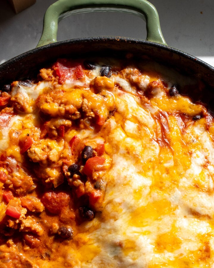 a green skillet full of cheesy chipotle chicken, beans, spicy sauce and lots of melted cheese.