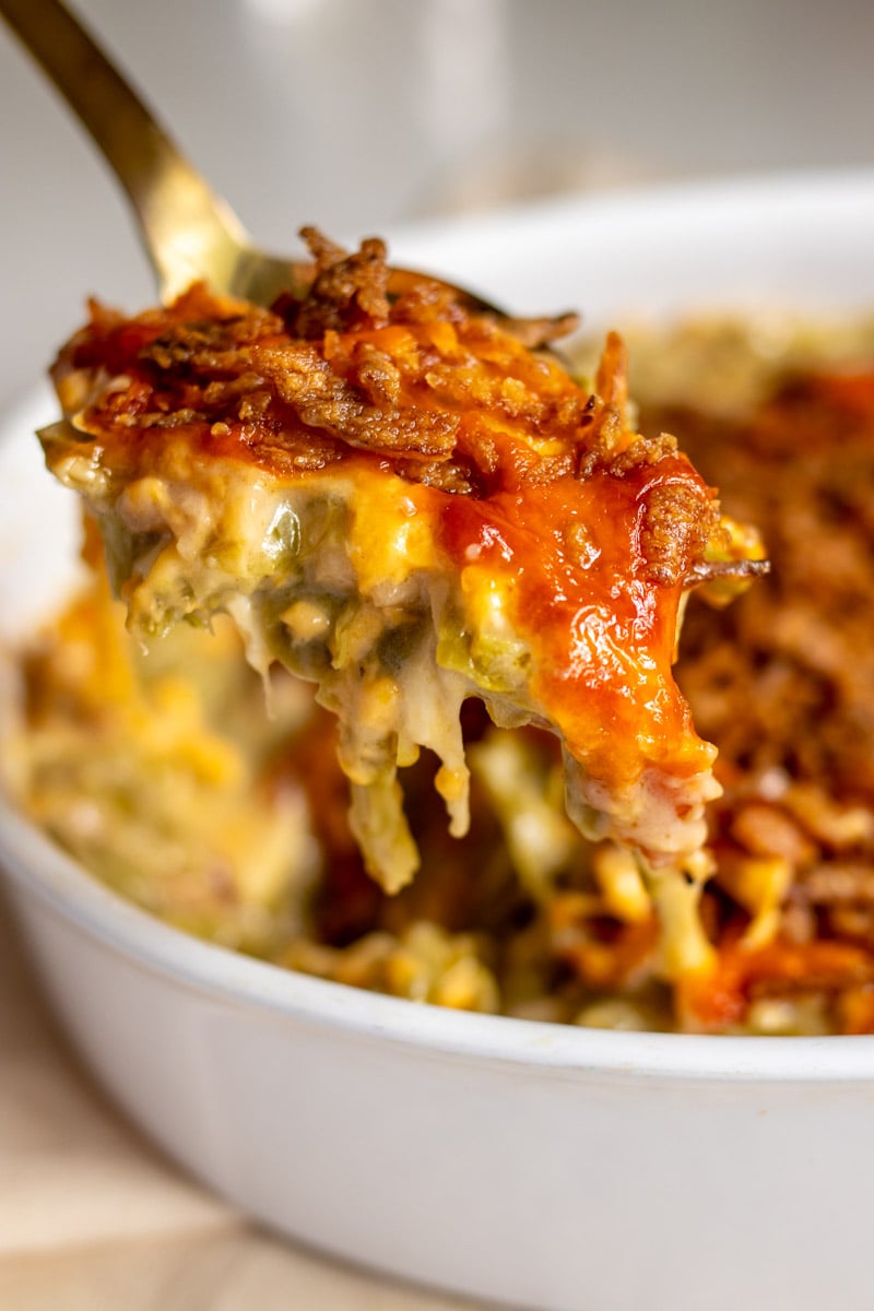 a serving spoon holding a scoop of cheesy green bean casserole. 