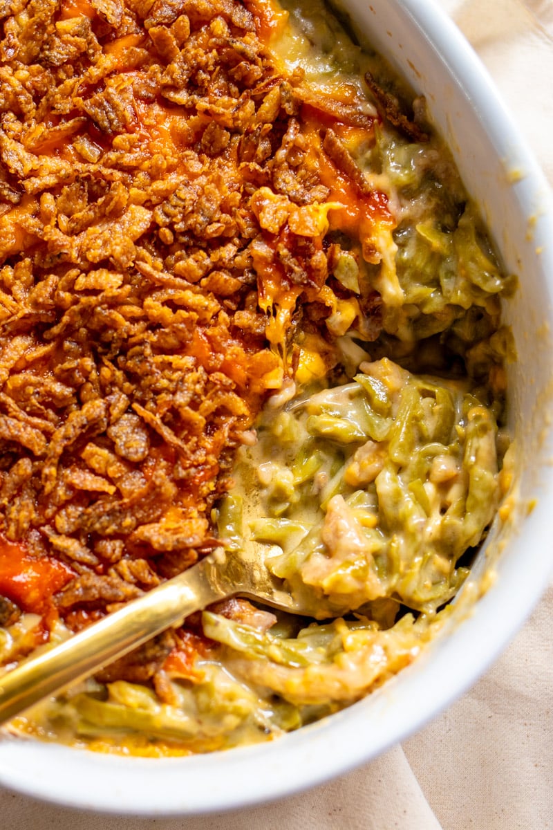 cheesy green bean casserole with a crispy onion topping in a white baking dish with a golden serving spoon.