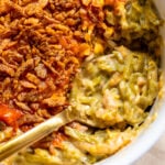 cheesy green bean casserole in a white baking dish with a golden spoon.