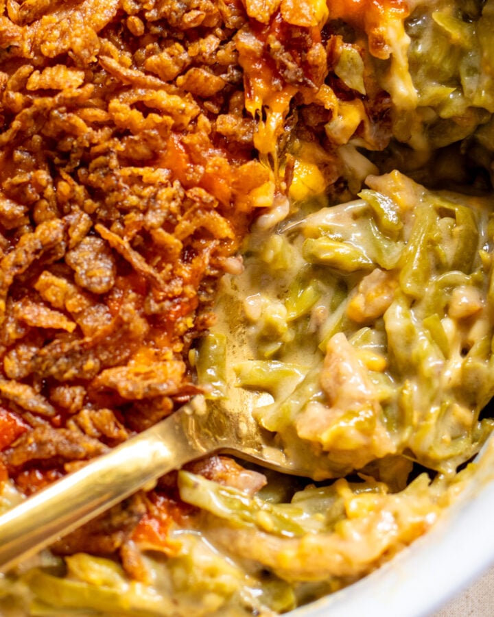 cheesy green bean casserole in a white baking dish with a golden spoon.