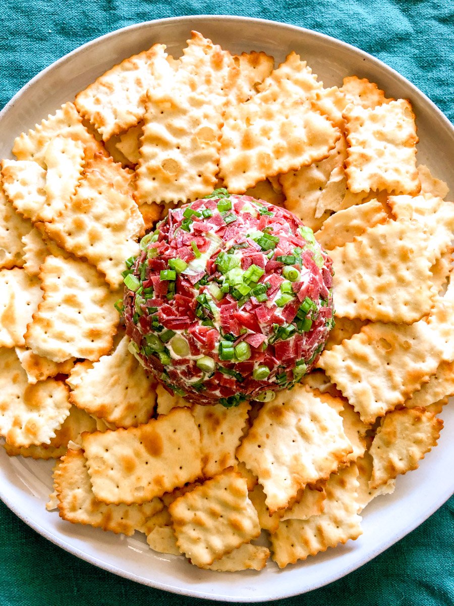 a dried beef cheese ball on a white plate surrounded by golden crackers.