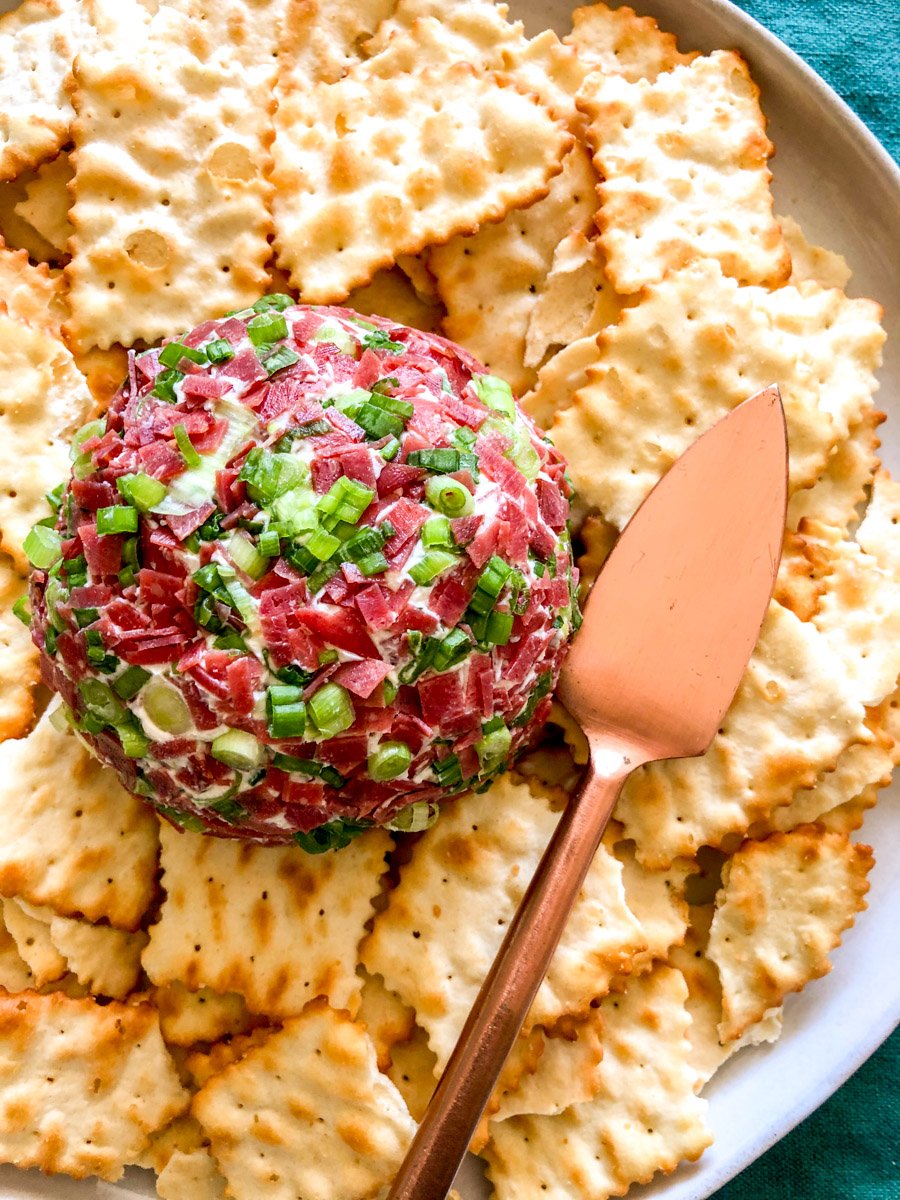 a dried beef cheese ball on a white plate surrounded by crackers.