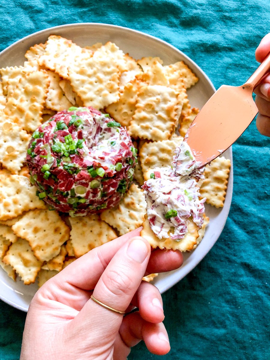 a hand holding a cracker getting smeared with dried beef cheese ball mixture. 