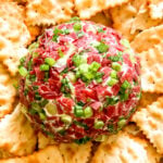 a cheese ball rolled in dried beef and green onion with ritz crackers surrounding it.