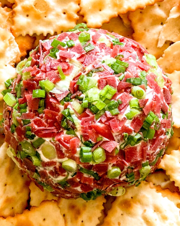 a cheese ball rolled in dried beef and green onion with ritz crackers surrounding it.