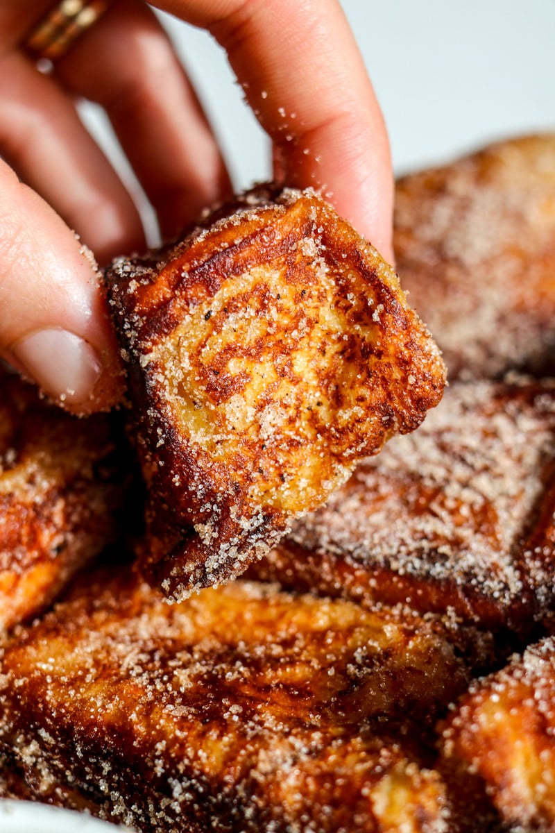 a hand holding a singular hawaiian roll french toast bite that's been rolled in cinnamon sugar. 