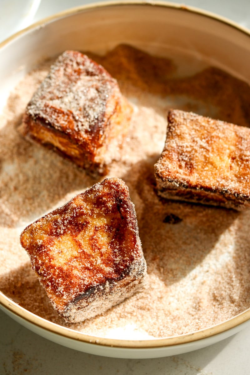 hawaiian roll french toast in a white bowl filled with cinnamon sugar.