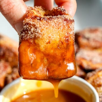 a hand holding a piece of hawaiian roll french toast dipping it into salted caramel.