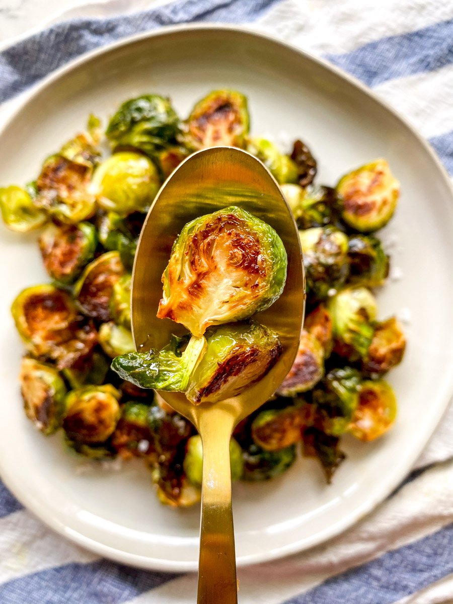 a golden spoon holding a singular crispy honey sriracha glazed brussels sprouts.