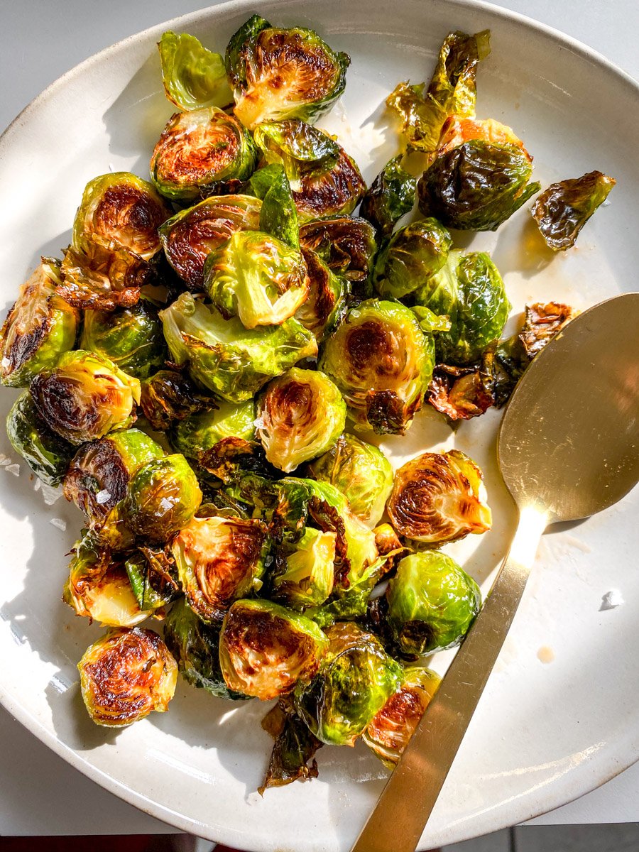 a white plate filled with honey sriracha brussels sprouts and a golden spoon.