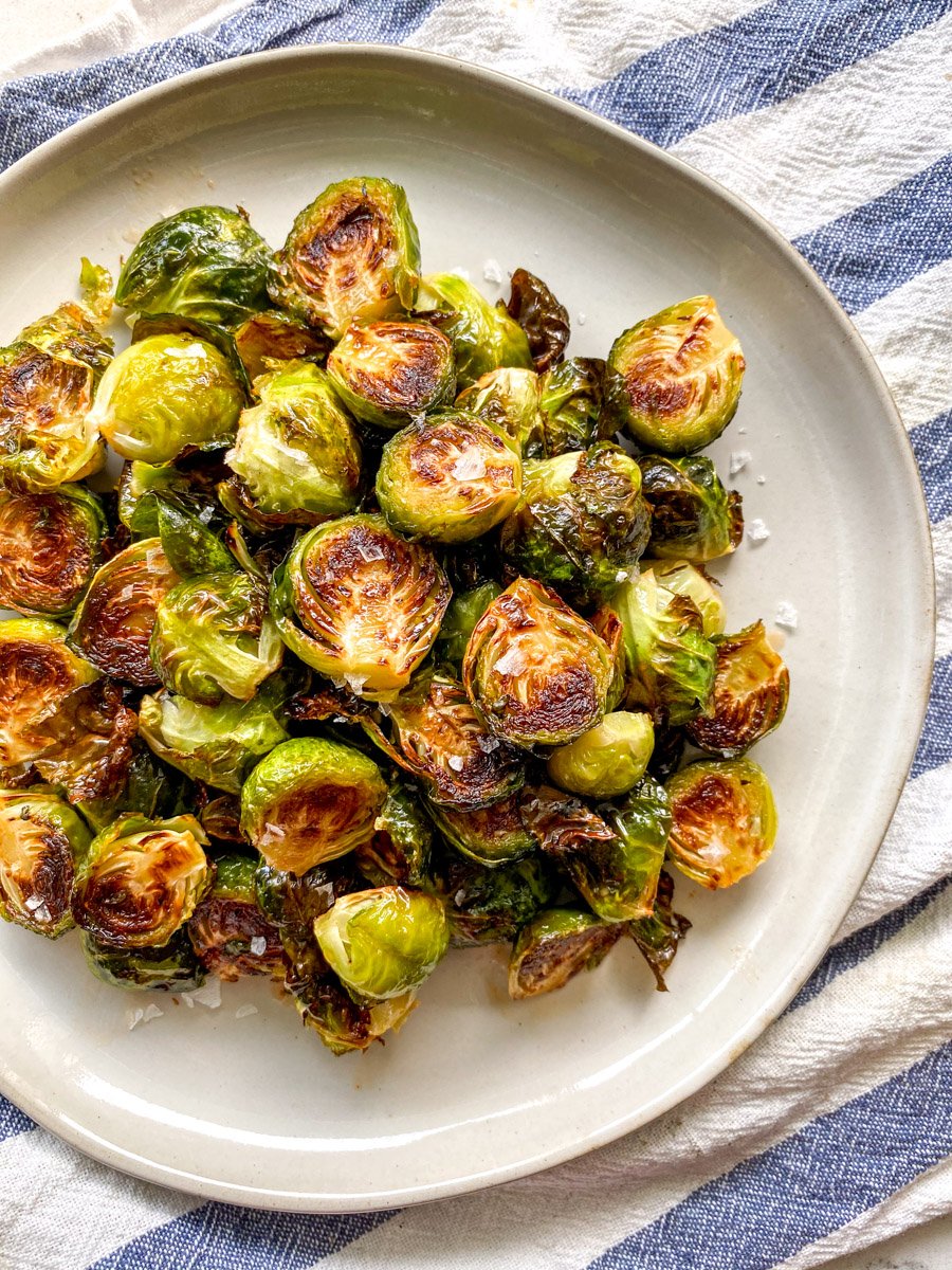 a white plate with honey sriracha brussels sprouts on a blue and white striped towel.