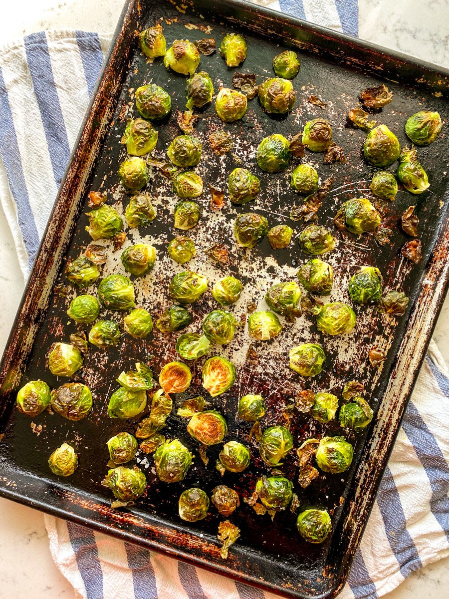 honey roasted sriracha brussels sprouts on a baking sheet with a blue and white striped towel underneath.