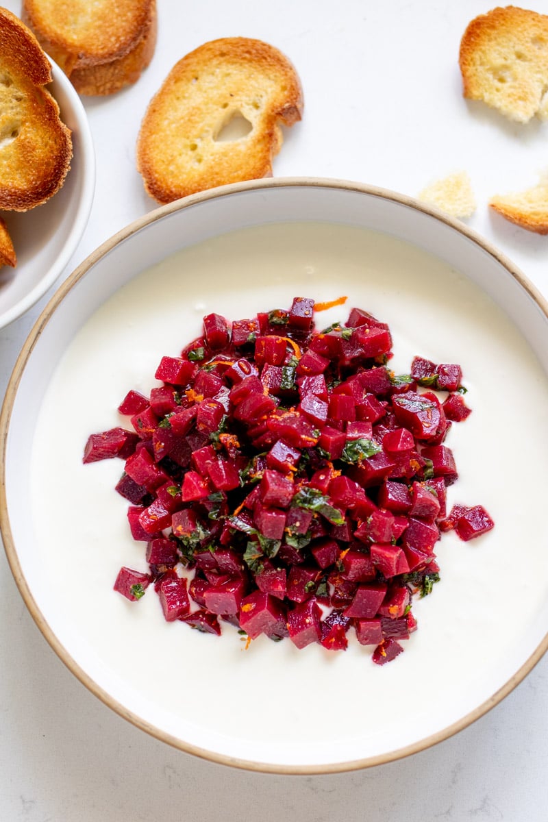 an overhead view of a white bowl filled with hot honey whipped feta and pickled beets with toasted baguettes around it. 