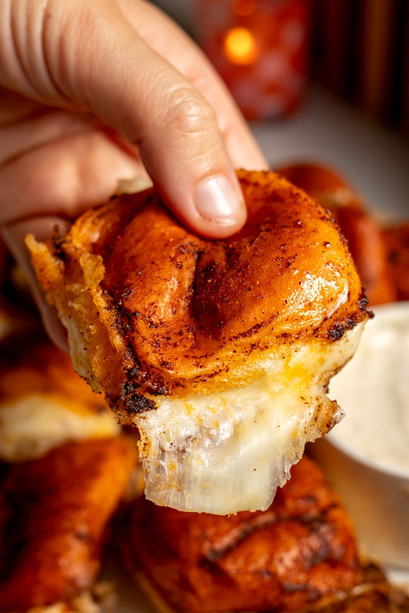 a hand holding a single soft hawaiian roll baked in nashville hot butter and stuffed with mozzarella cheese.