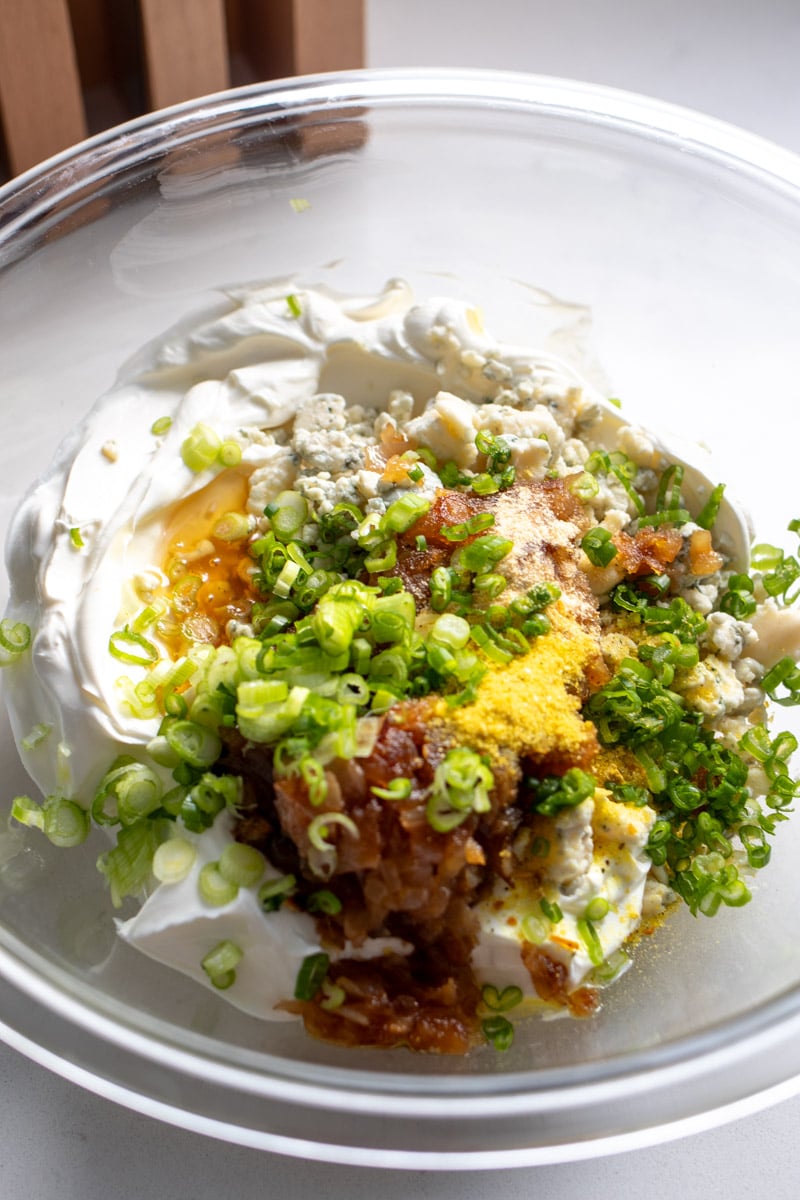 all the ingredients of caramelized onion dip in a glass bowl on a white countertop. 