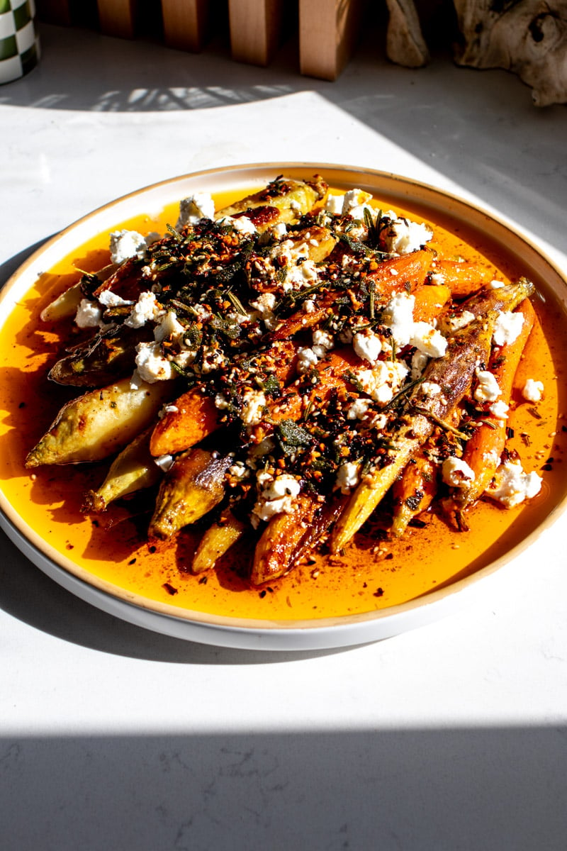 a white serving platter filled with roasted carrots and crispy chili oil. 