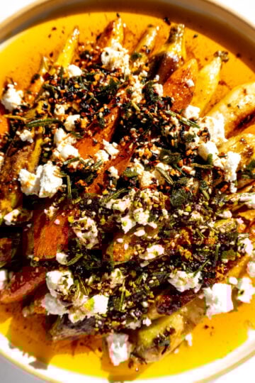 a white plate topped with roasted carrots and thanksgiving crispy chili oil with crispy fried bits of sage, rosemary and thyme.