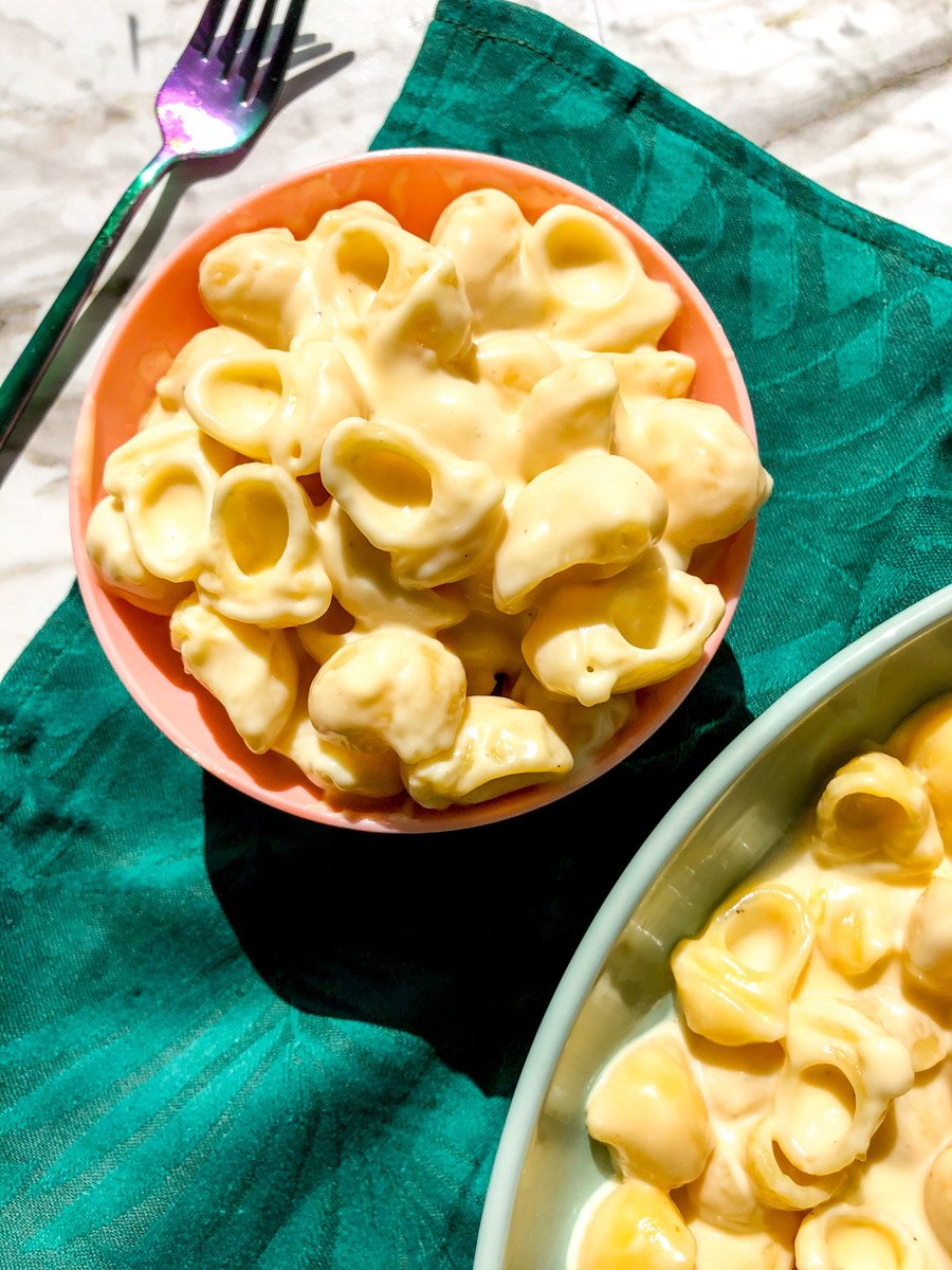 a pink serving bowl and a blue platter both full of white cheddar mac and cheese.