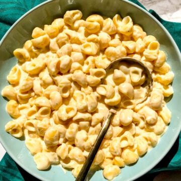 a blue bowl filled with white cheddar mac and cheese with a golden spoon.