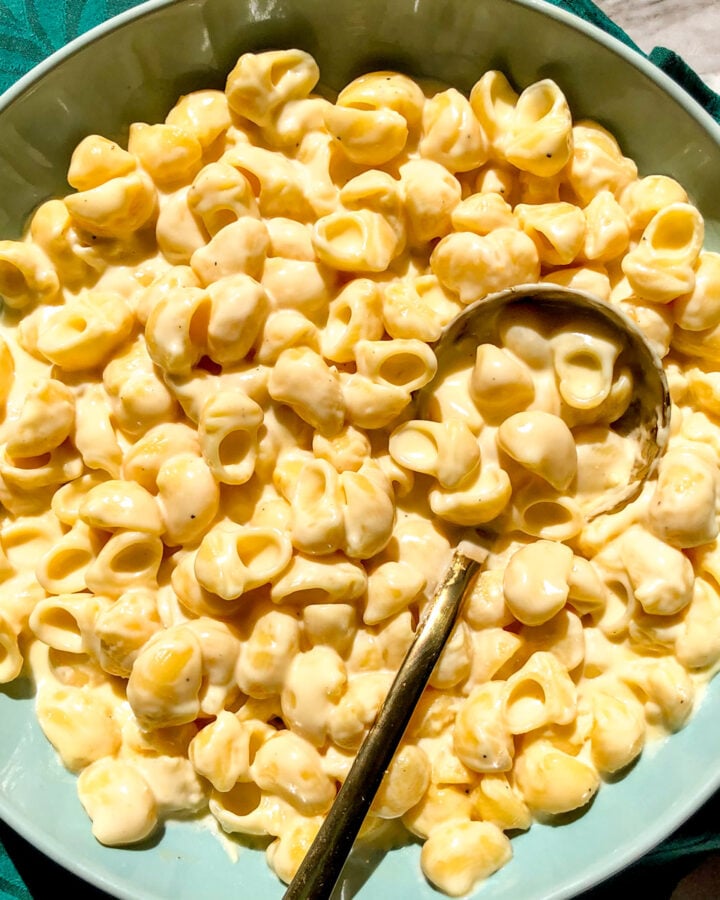 a blue bowl filled with white cheddar mac and cheese with a golden spoon.