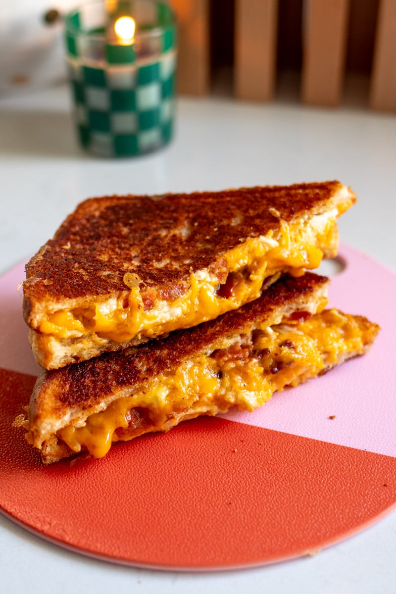 a grilled cheese sandwich cut in half sitting on top of each other on a pink and red cutting board.