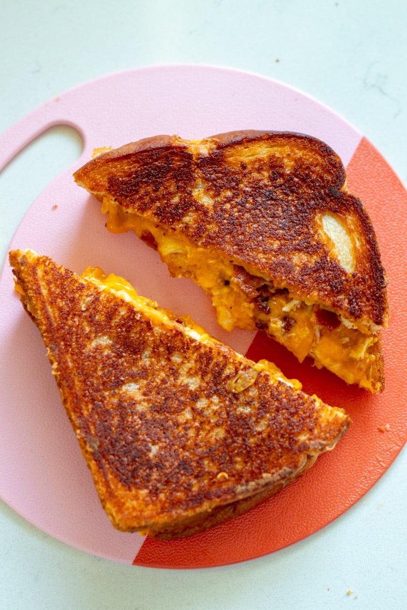 a pink and red circular cutting board with a split open grilled cheese on it.