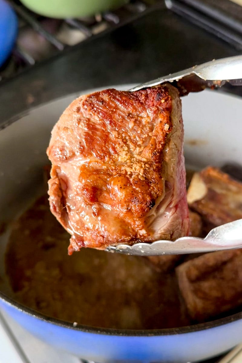 a crispy golden seared short rib being held by a pair of tongs. 