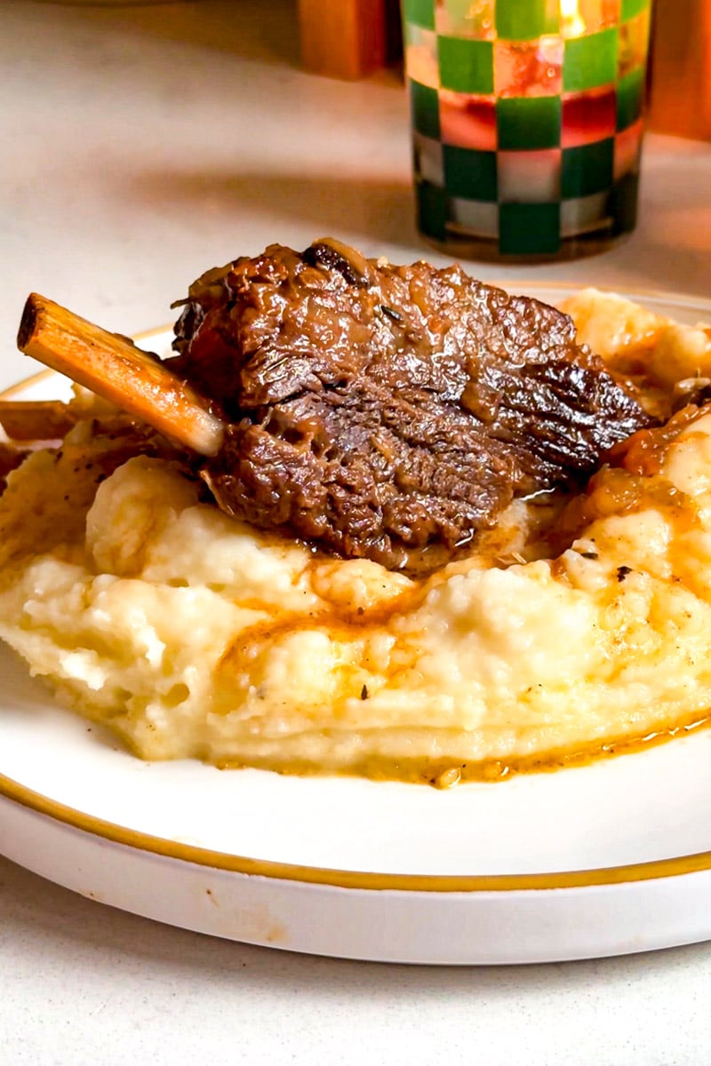 a singular short rib with the bone attached over mashed potatoes with brown gravy.